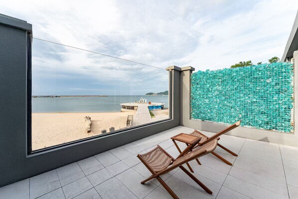 A balcony with a view of the beach, a wooden chair, and a small table. - Bay Four Seasons Castle Hotel (Weihai)