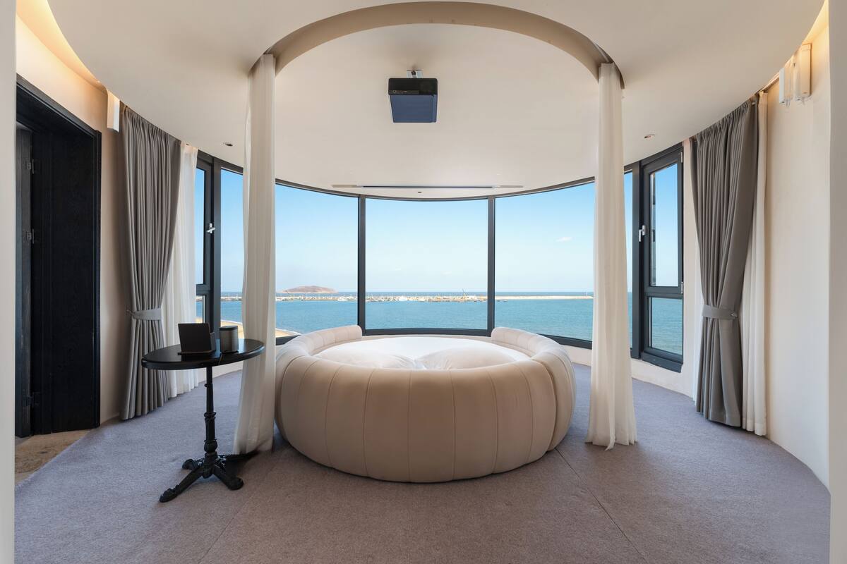 A room with a large circular seating area, a small table, and a ceiling-mounted projector.