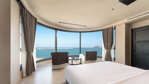 A modern hotel room with a large bed, two armchairs, a small table, and a view of the sea. - Bay Four Seasons Castle Hotel (Weihai)