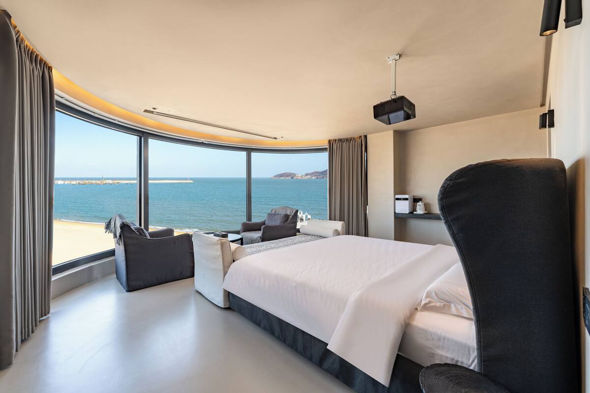 A modern hotel room with a large bed, seating area, and a view of the sea.