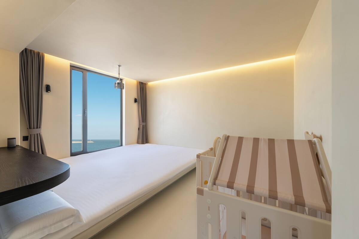 A modern hotel room with a large window, a bed, a small table, and a striped chair.