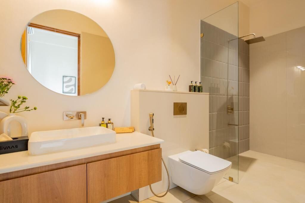 Un bagno moderno con uno specchio rotondo, un lavandino bianco, un water e un box doccia in vetro.