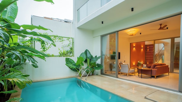 Una piscina interior con pared de vidrio que conecta con una sala de estar con sofá y mesa.