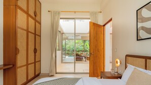 Habitación de hotel con cama, mesita de noche, armario de madera y puerta corrediza de vidrio que da a un balcón.