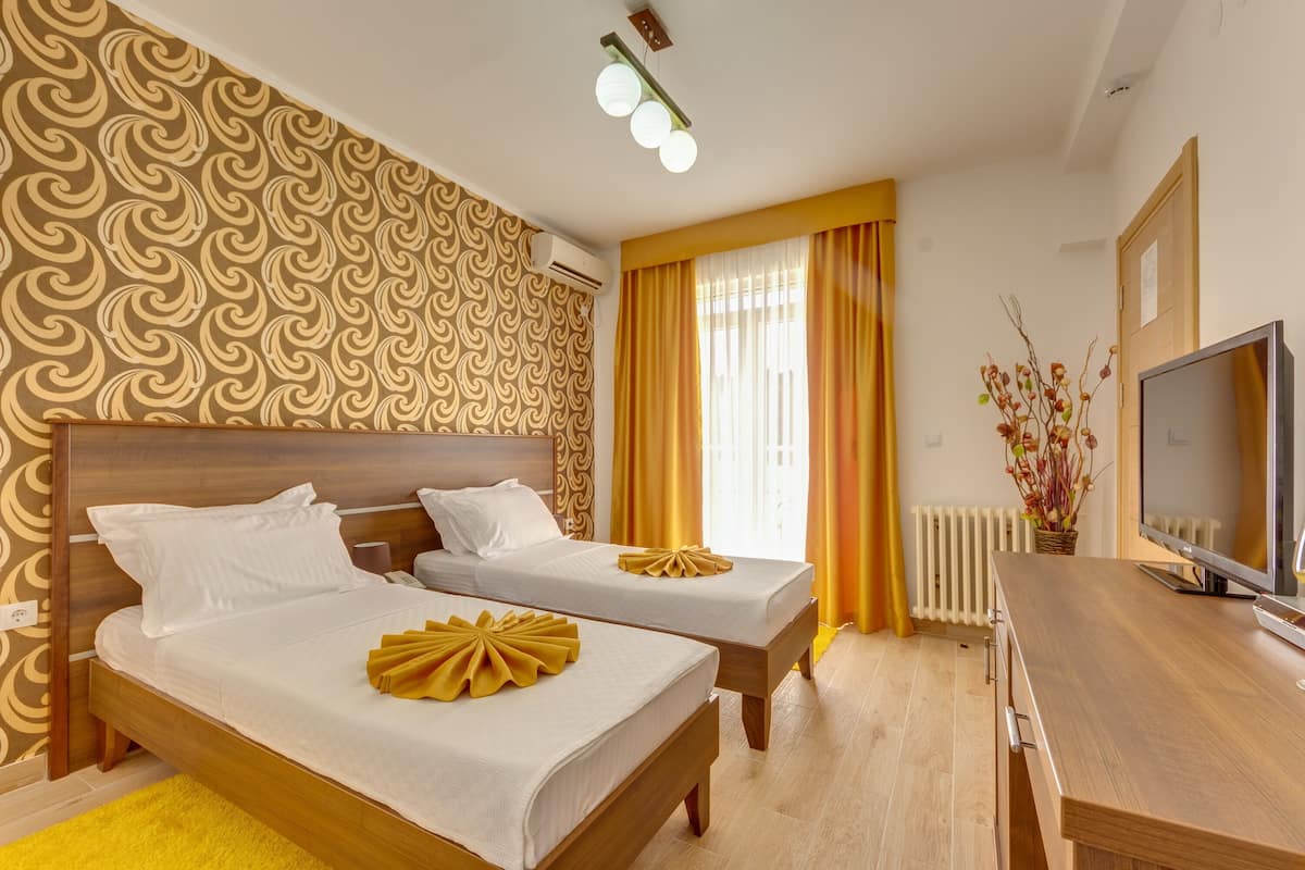 A hotel room with two beds, a TV, a wooden desk, and a window with curtains.