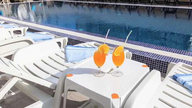 Zona de piscina con sillones de descanso y una mesa con dos bebidas.