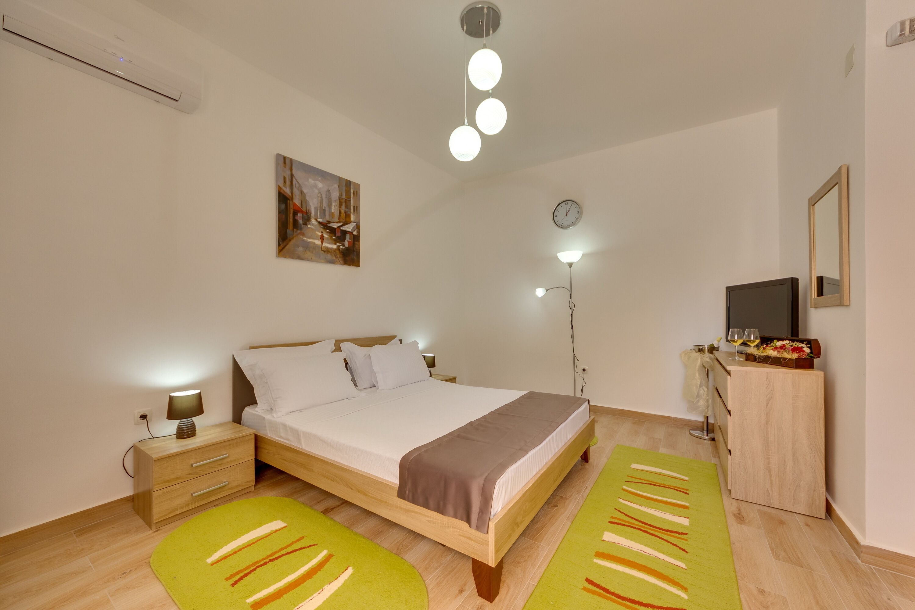 A bedroom with a bed, bedside table, lamp, dresser, mirror, clock, and artwork.