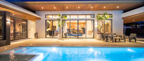 Una casa moderna con piscina, amplios ventanales y mobiliario de exterior.