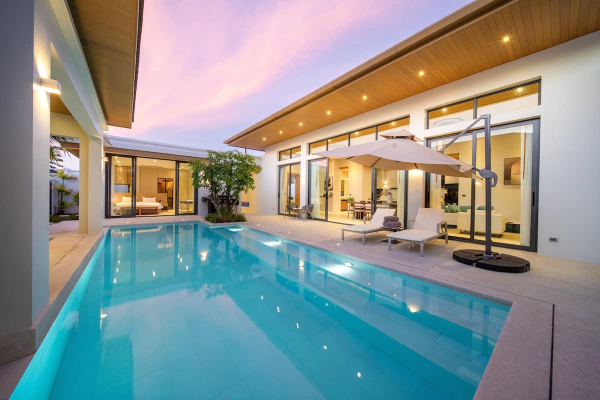 Ein moderner Poolbereich mit klarem, blauem Wasser, Liegestühlen und einem wintergartenartigen Essbereich.