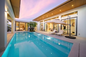 Ein moderner Poolbereich mit klarem, blauem Wasser, Liegestühlen und einem wintergartenartigen Essbereich.