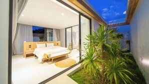 A modern bedroom with a large bed, a bedside table, and a view of the outdoors. - Ming Resort Phuket (Mai Khao)