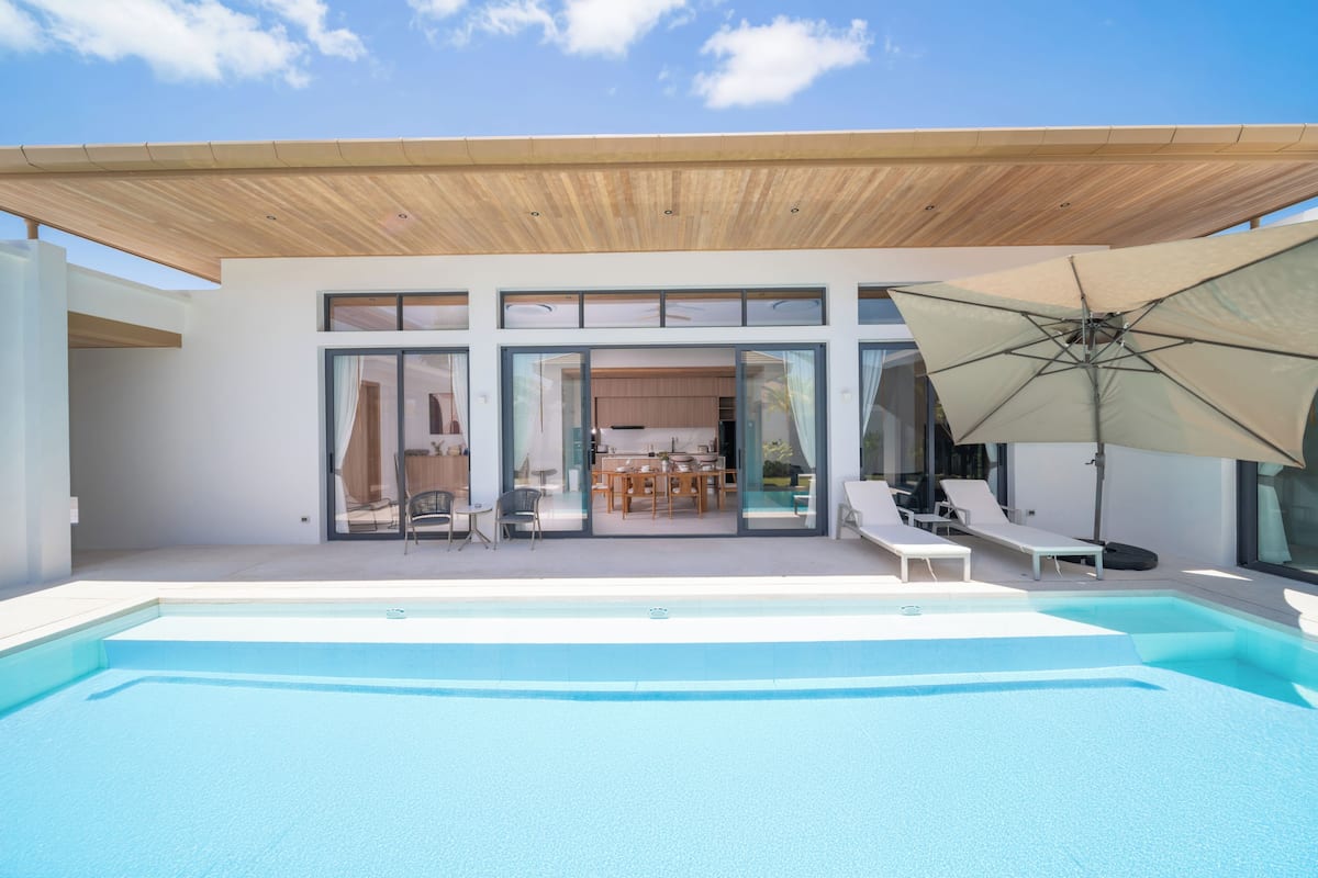 Ein moderner Poolbereich mit einer Holzhütte, einem Pool und einem Essbereich, der durch Glastüren sichtbar ist.