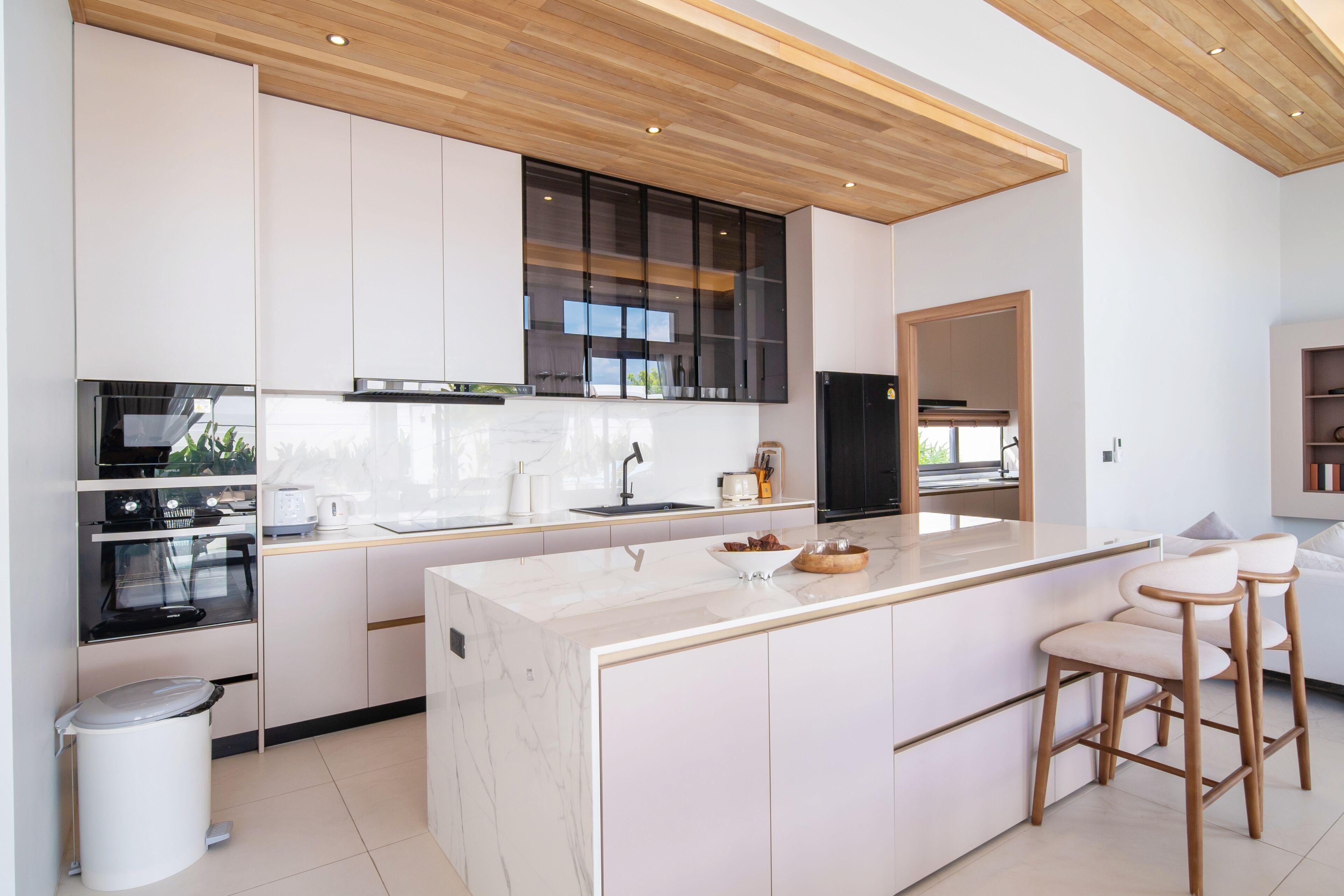 Una cocina moderna con armarios blancos, una isla de mármol y taburetes de madera.