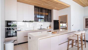 Una cocina moderna con armarios blancos, una isla de mármol y taburetes de madera.