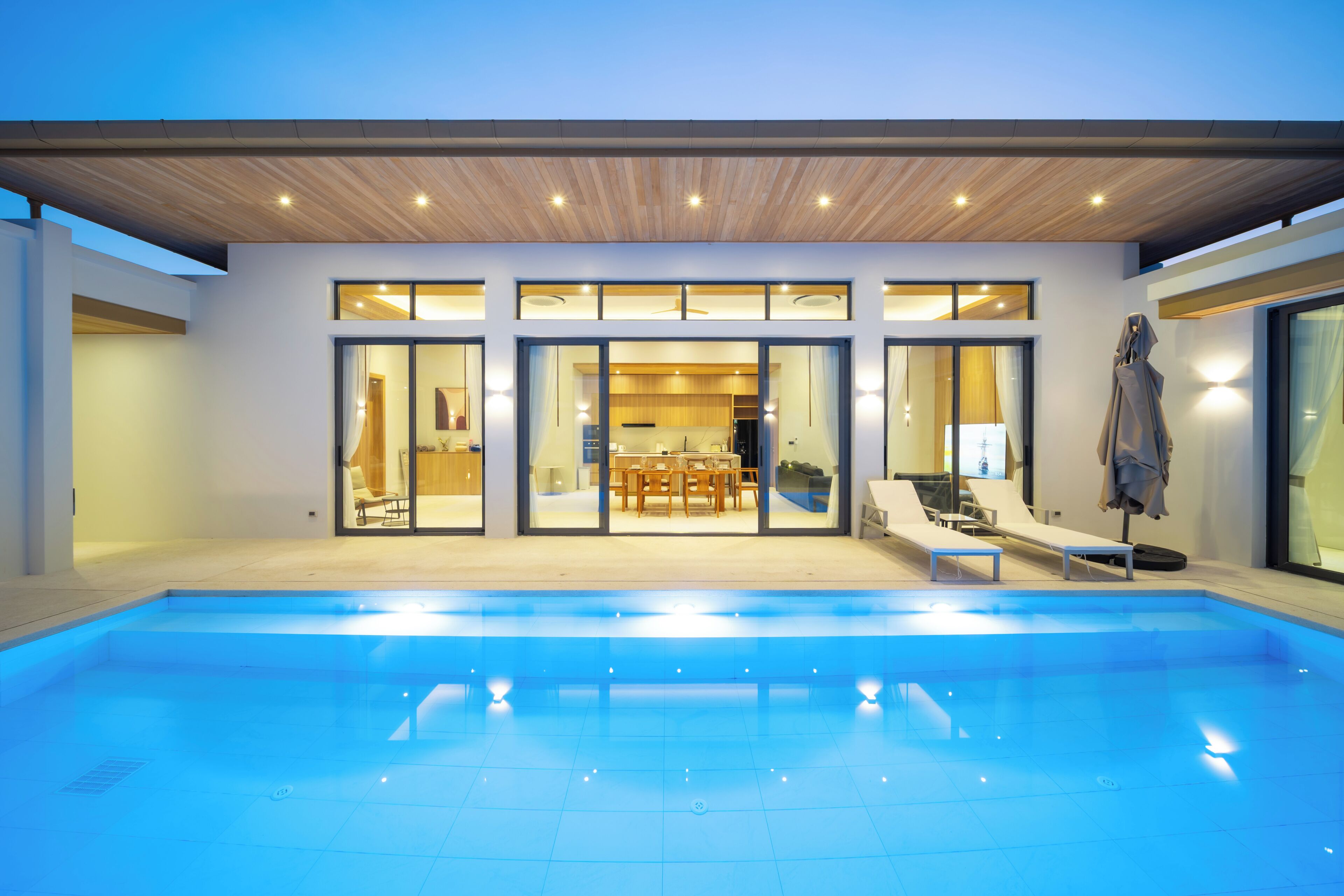 A modern house with a swimming pool, large windows, and a dining area.