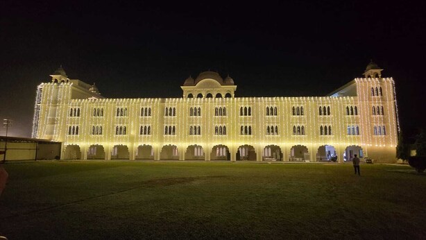 A large, illuminated building with multiple arched windows and a central dome, surrounded by a grassy courtyard. - Hotel Shravan Royal Inn  (Jaipur)