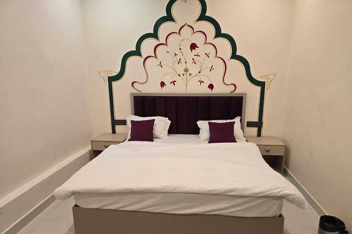A bedroom with a large bed, two nightstands, a decorative headboard, and a trash can.