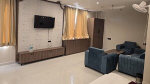 A modern living room with a flat-screen TV, a sofa, a coffee table, and a ceiling fan. - Hotel Shravan Royal Inn  (Jaipur)