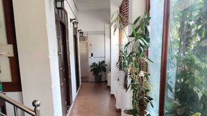 A hallway with marble flooring, potted plants, and a view of greenery through a window. - WHITE FORT THEKKADY (Kumily)