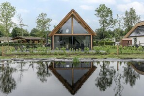 Una casa moderna con un tetto triangolare, ampie vetrate e un riflesso in uno stagno.