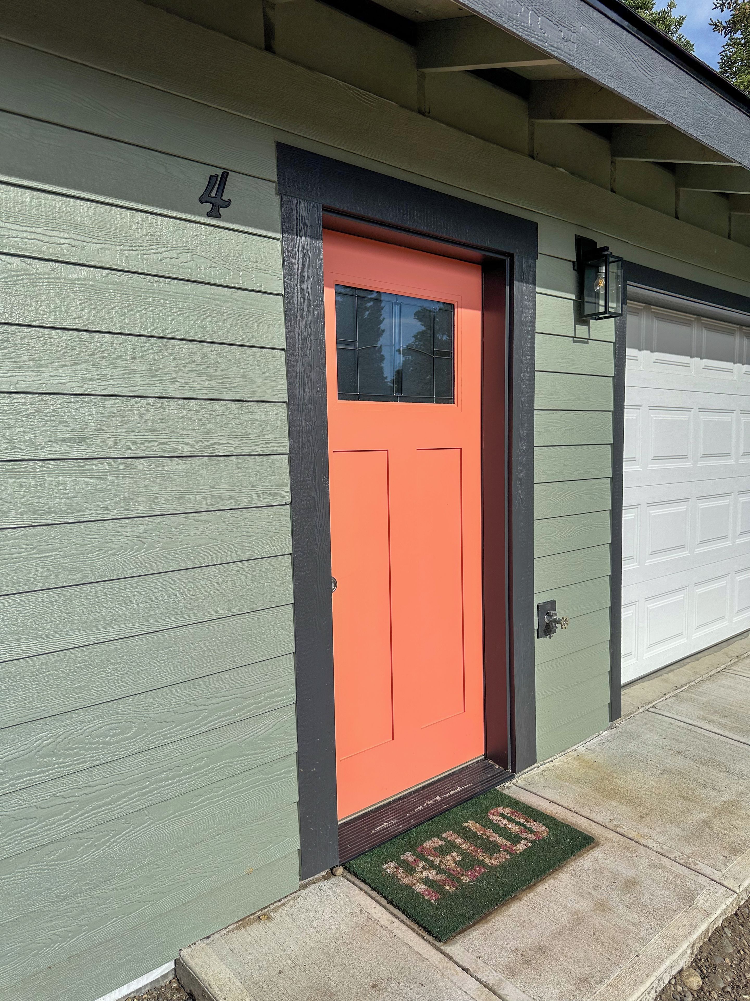 A house with a green siding exterior, a red door, and a garage door.