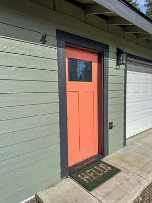 A house with a green siding exterior, a red door, and a garage door. - Quaint 2-bedroom house in welcoming Kenai for your getaway (Kenai)