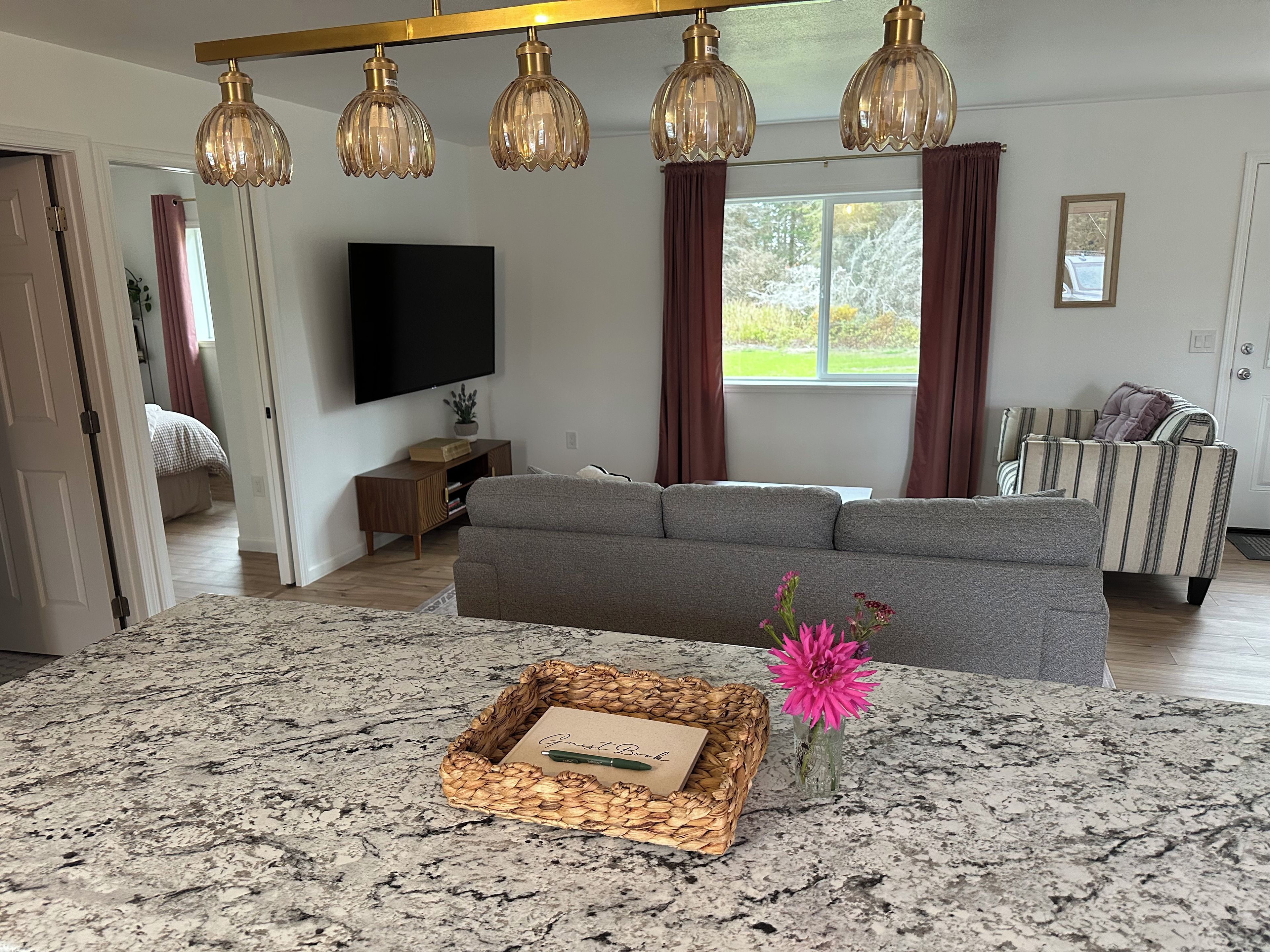 A modern living room with a grey sofa, a flat-screen TV, a wooden side table, and a decorative basket on a granite countertop.