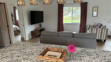 A modern living room with a grey sofa, a flat-screen TV, a wooden side table, and a decorative basket on a granite countertop.
