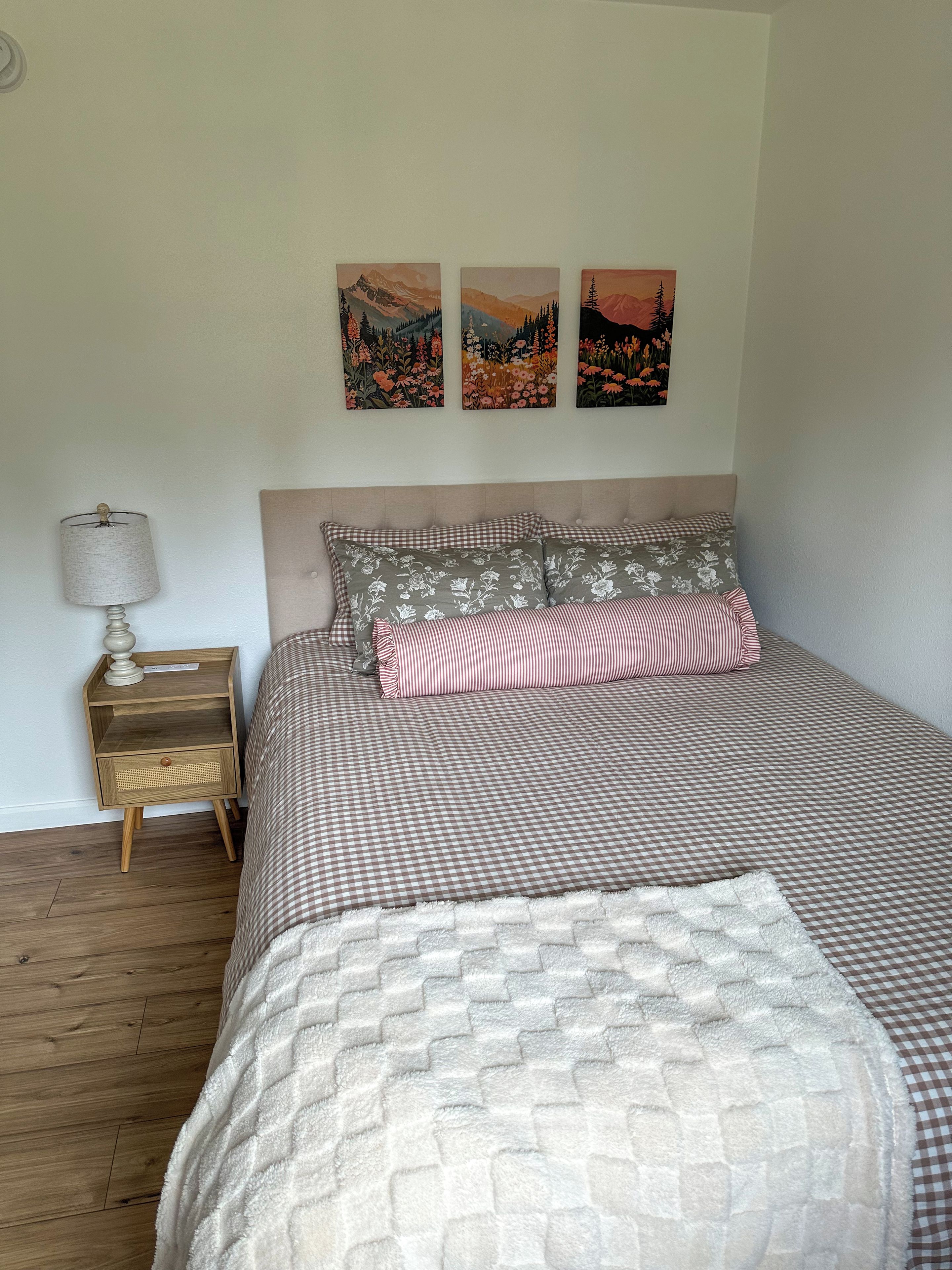 A bedroom with a bed, a nightstand, a lamp, and three wall-mounted paintings.