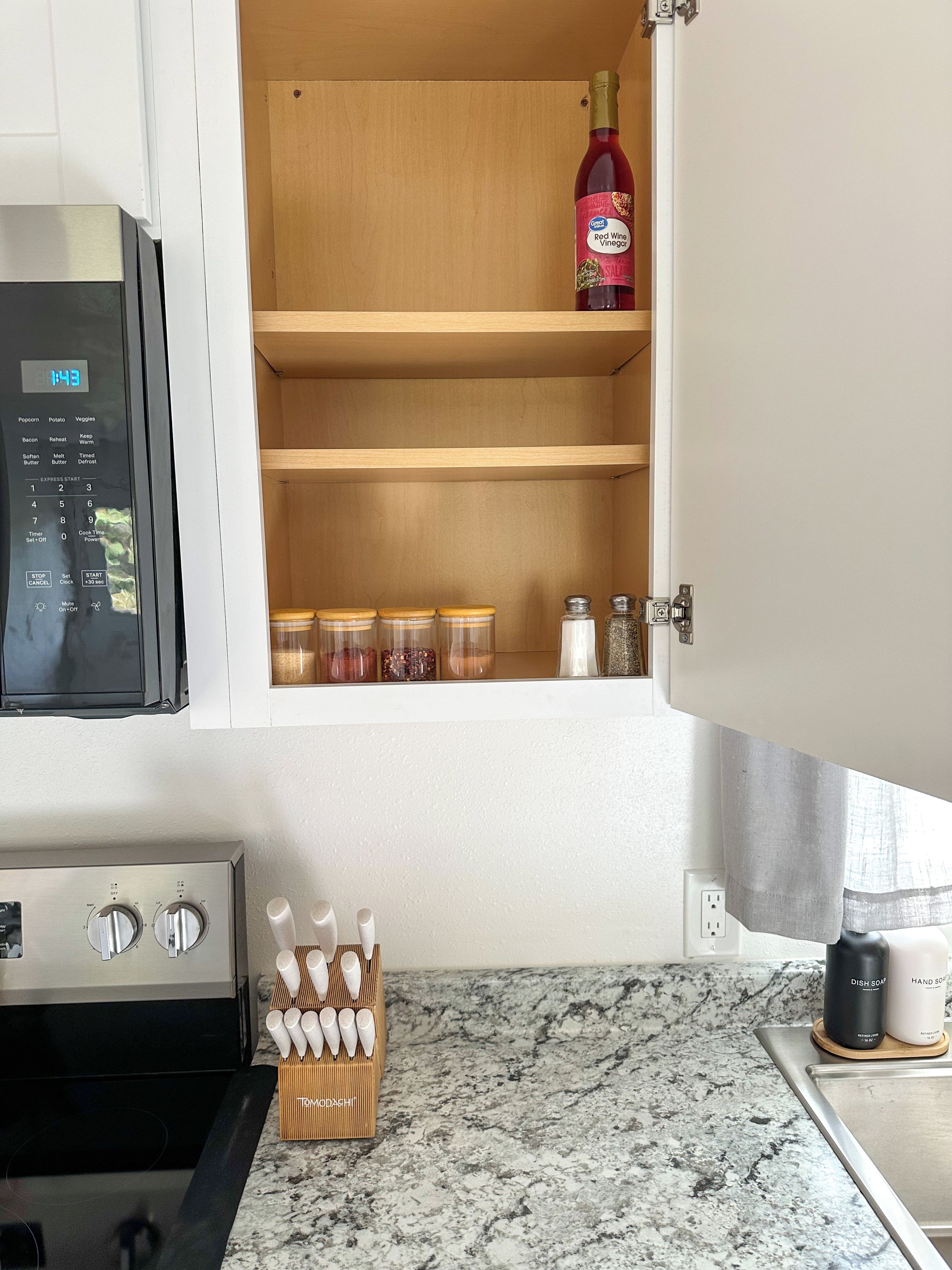 A kitchen with a microwave, a spice rack, and a bottle of red wine vinegar.