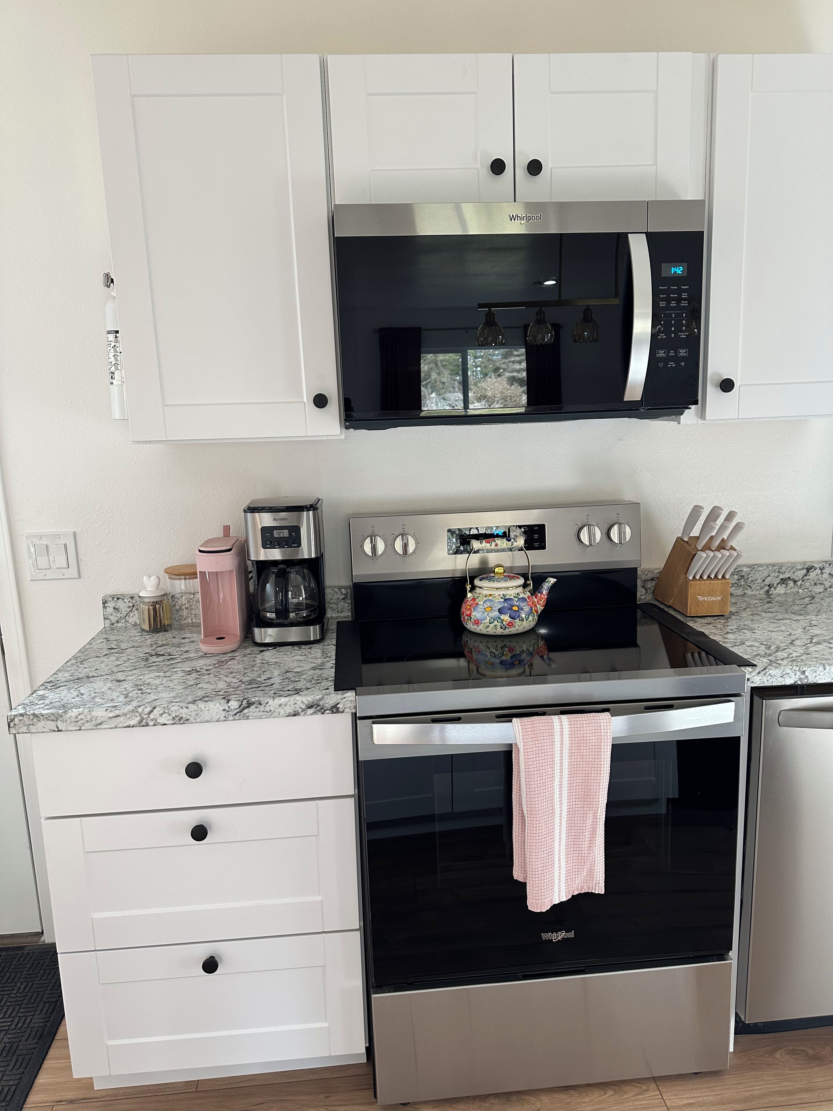 A compact kitchen with a microwave, stove, and oven, featuring white cabinetry and a marble countertop.
