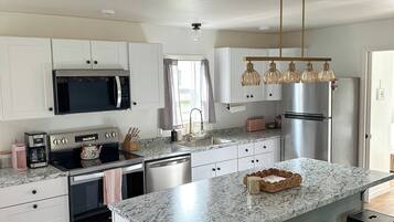 A modern kitchen with white cabinets, stainless steel appliances, a granite countertop, and a bar stool area.
