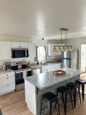 A modern kitchen with white cabinets, stainless steel appliances, a granite countertop, and a bar stool area. - Quaint 2-bedroom house in welcoming Kenai for your getaway (Kenai)
