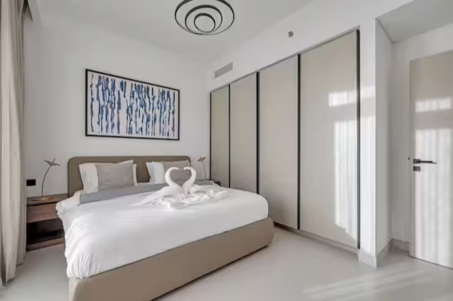 A modern bedroom with a large bed, a wall-mounted artwork, a wardrobe, and a door.