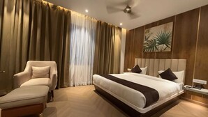 Quarto de hotel moderno com uma cama grande, um chaise longue, um ventilador de teto e uma janela ampla com cortinas.