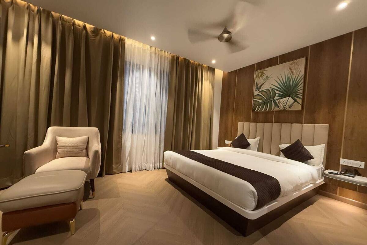Habitació d'hotel moderna amb un llit gran, un divan, un ventilador de sostre i una finestra ampla amb cortines.