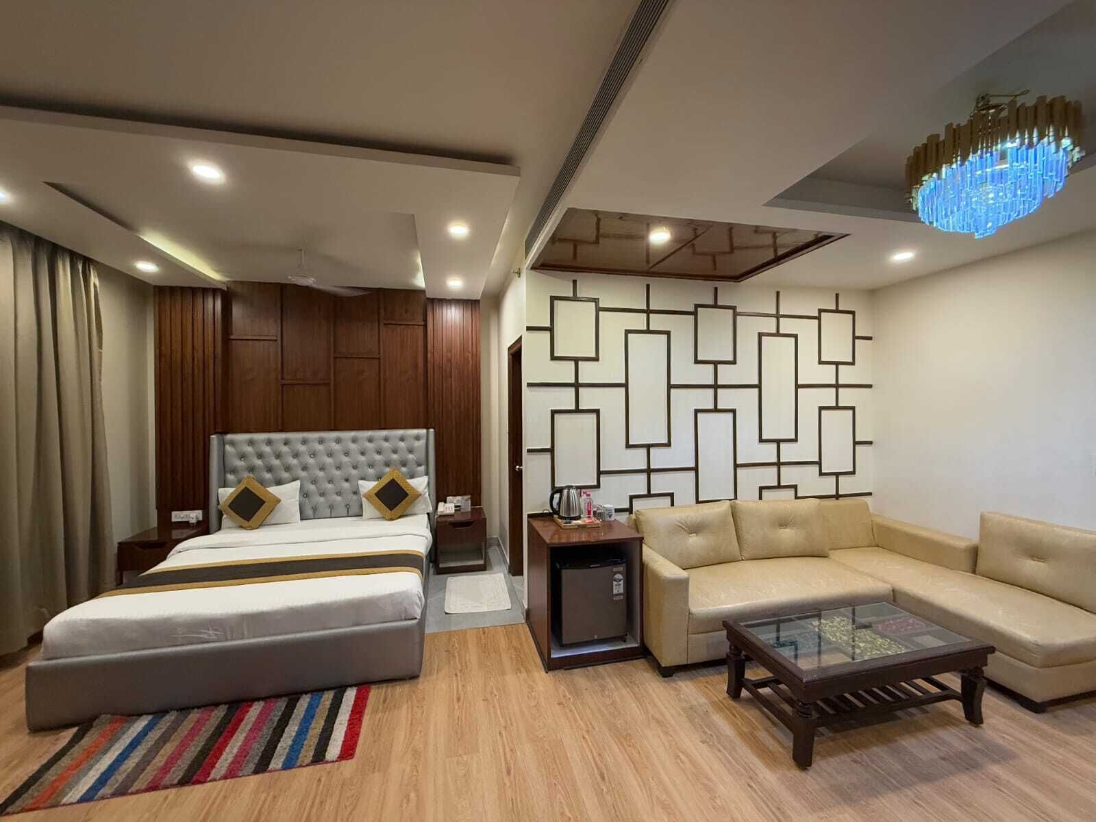 A modern hotel room with a large bed, a sofa, a coffee table, a small TV, and a decorative wall panel.
