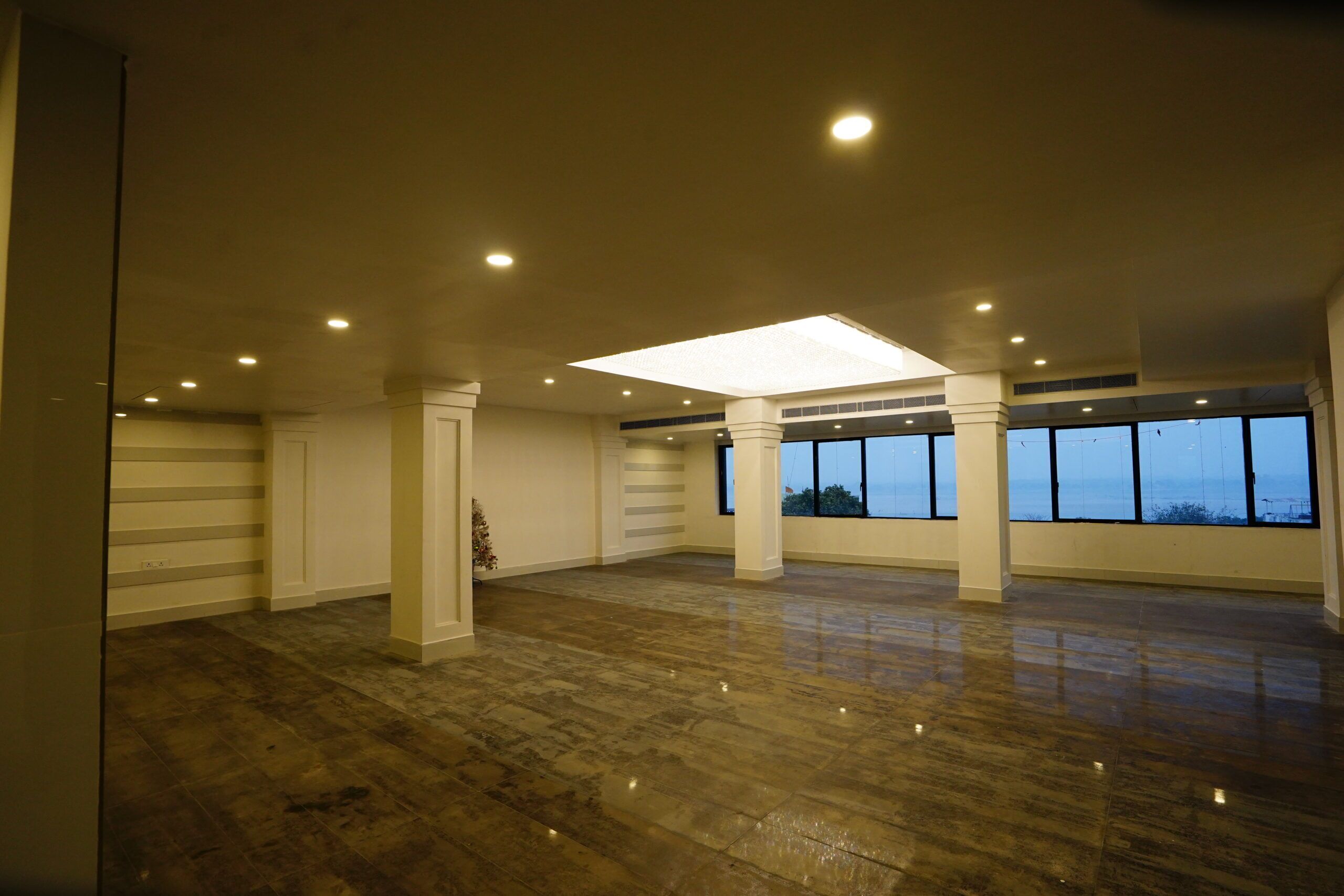 A spacious room with a polished wooden floor, large windows, and a central ceiling light.