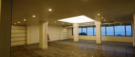 A spacious room with a polished wooden floor, large windows, and a central ceiling light.