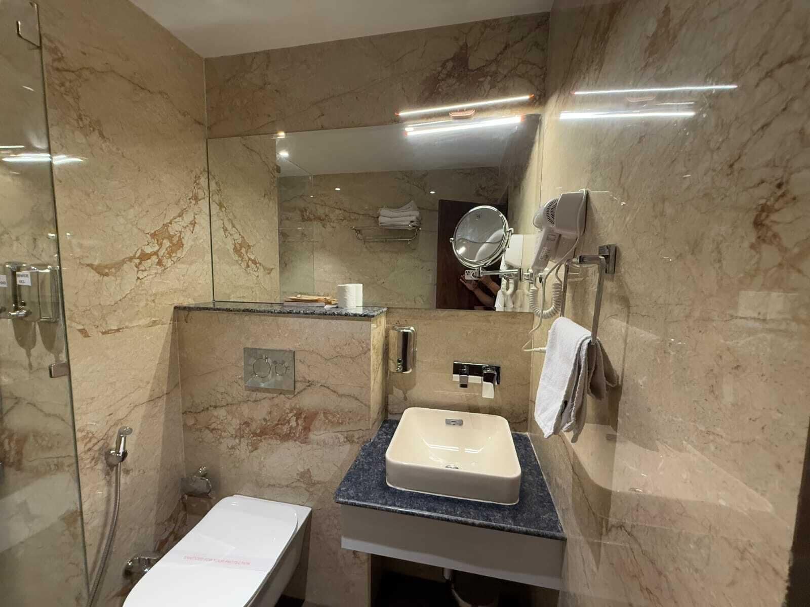 A bathroom with a marble wall, a sink, a mirror, a handheld showerhead, and a towel rack.