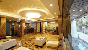 Um hall amplo com piso de mármore, balcão de recepção, área de estar e um grande lustre circular.