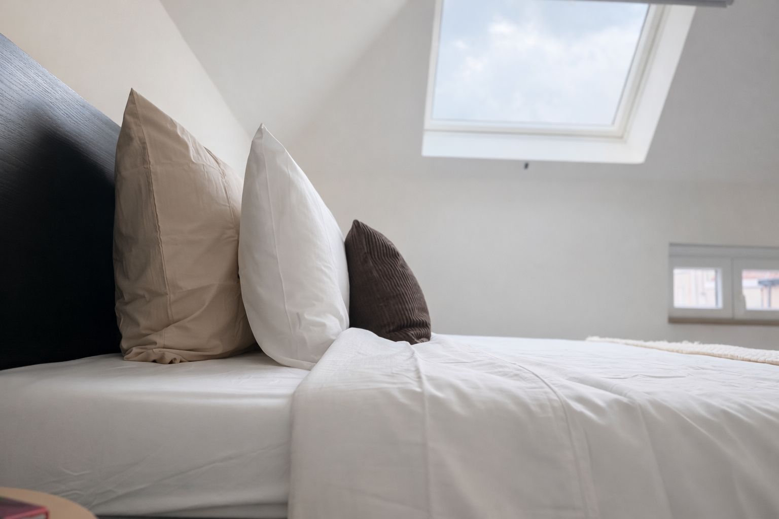 Un lit avec une literie blanche et trois oreillers de couleurs différentes.
