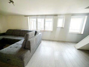 A room with a grey sectional sofa, large windows, and a wooden floor. - Central Ghent | Modern 6BR Apt. w/ WIFI (Ghent)