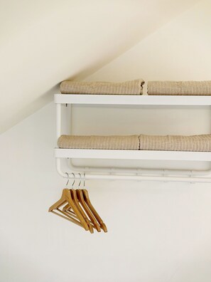 Een witte muur met een wit wandrek met daarin twee beige kussens en een houten hanger.
