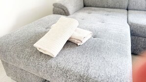 En grå soffa med en hopvikt vit handduk på.