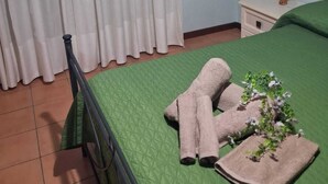 A room with a green bedspread, a pair of towels, a small table with a lamp, and a framed picture on the wall. - Cottage a stone's throw from the sea (San Vito Lo Capo)