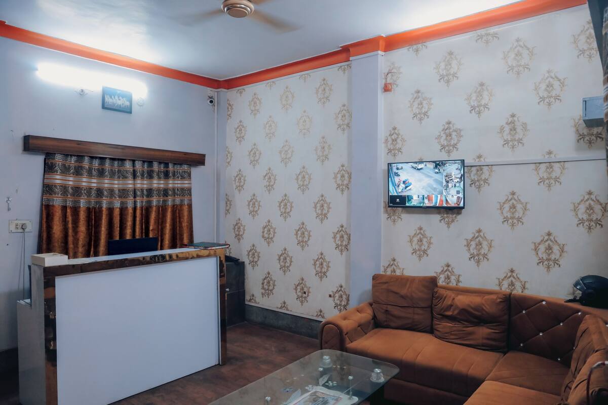 Una recepción, un sofá marrón, un televisor montado en la pared y un papel tapiz estampado.
