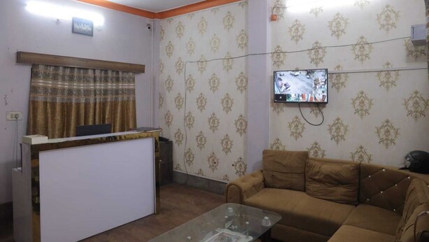 A living room with a sofa, a television mounted on the wall, and a patterned wallpaper. - Hotel The TWB Palace (Gwalior)