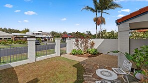 A residential backyard with a stone patio, outdoor furniture, a white fence, and a palm tree. - Baillie s Getaway - Lifestyle Yamba (YAMBA)