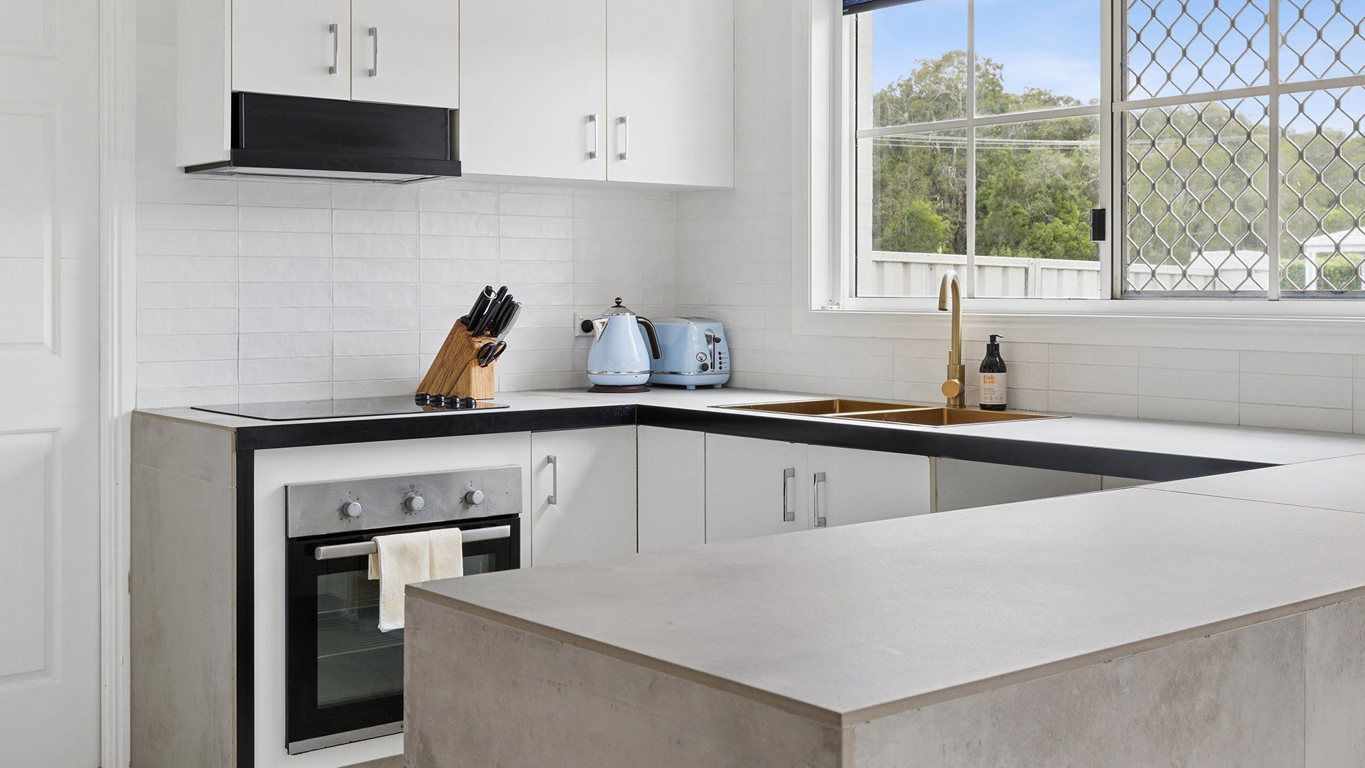 A modern kitchen with white cabinetry, a black countertop, a built-in oven, and a window with a view of greenery.
